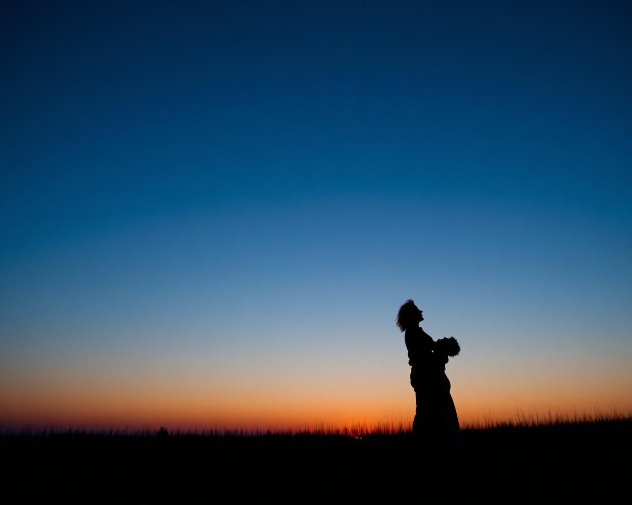 Couple silhouetted against a deep blue and orange sunset sky in an open field