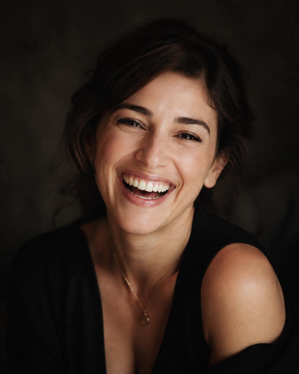 Woman laughing warmly in soft natural light against a dark backdrop